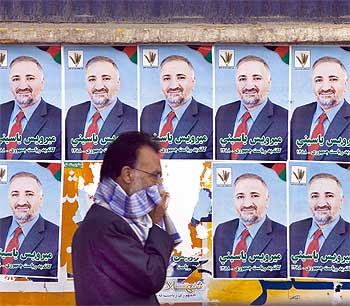 A man covers his face during a sandstorm while he walks past election posters of Mirwais Yasini, a presidential candidate, in Kabul.