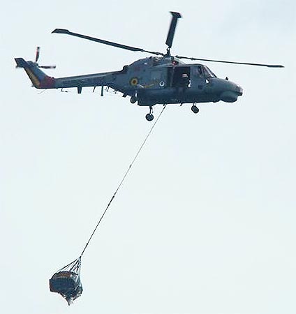 A helicopter transports to a ship a piece of debris.