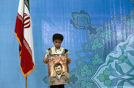 A supporter of Ahmadinejad holds a campaign poster as he stands next to the Iranian flag during an election campaign at a stadium in Tehran