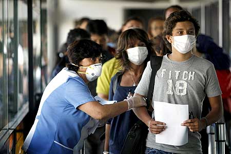A health worker (L) wearing a mask monitors passengers arriving from Mexico and coming through Peru for possible H1N1 flu infection at Santiago's international airport on April 27