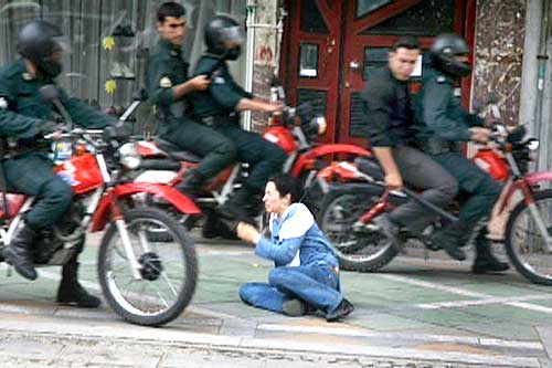 Security personnel look at a woman sitting on the ground as they ride past in Tehran