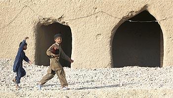 A boy carries a rooster as he walks while a girl runs behind near a checkpoint