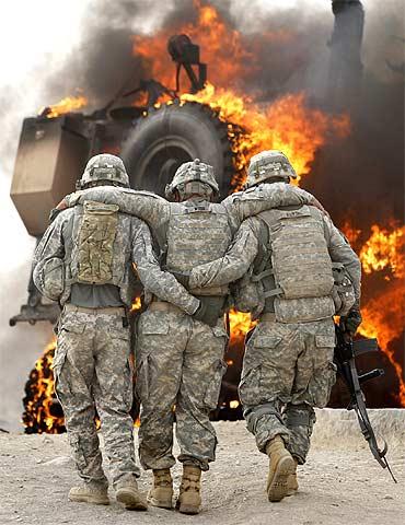 An injured soldier from the US army is assisted past a burning vehicle