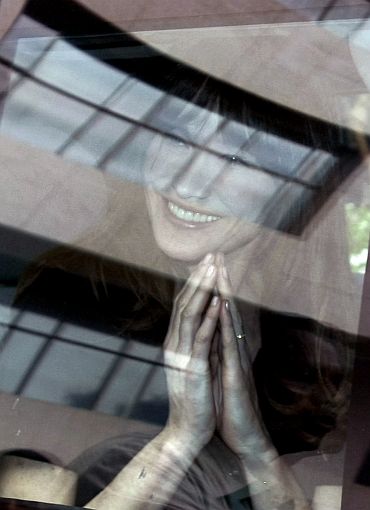 France's First Lady Carla Bruni-Sarkozy clasps her hands together in the traditional Indian welcome through the window of her car