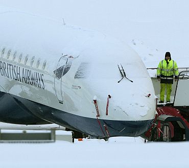 An engineer stands next to a snow covered British Airways aeroplane at Edinburgh Airport, in Edinburgh, Scotland