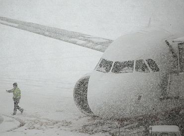 A worker walks past a plane parked on the snow covered tarmac of Zurich airport