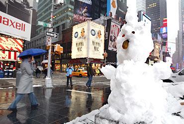 A snowman with a pickle nose and eyes made of pennies sits in Times Square in New York