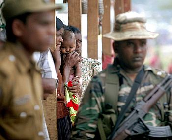 Members of the armed forces stand guard near internally displaced people (IDPs) who are living at the Ananda Kumarswami camp at Manik Farm in northern Sri Lanka