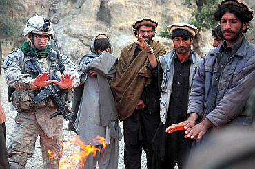 A US oldier warms his hands by a fire alongside locals in the Zanbar province of Afghanistan