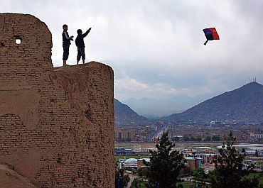 Boys fly a kite from a crumbling wall in Kabul