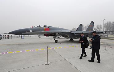 Foreign military delegates walk past a Jian-11 fighter jet on display in Beijing