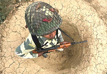 -A Border Security Force soldier stands in a trench as he guards the fenced border with Pakistan