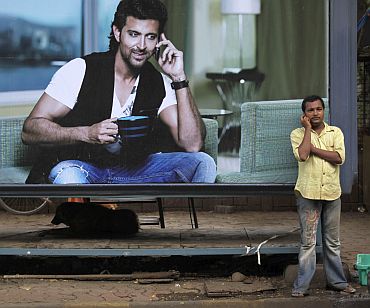 A man makes a phone call on his mobile phone in front of an advertisement for Reliance in Mumbai
