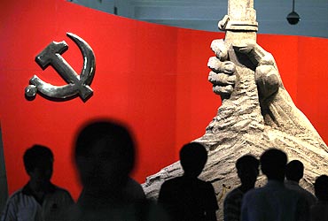 Visitors are silhouetted in front of a statue of a hand holding a gun next to a Chinese Communist Party flag at the Chinese Military Museum in Beijing