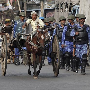 Rapid Action Forces personnel patrol a road as a man on a horse cart passes by in Ayodhya