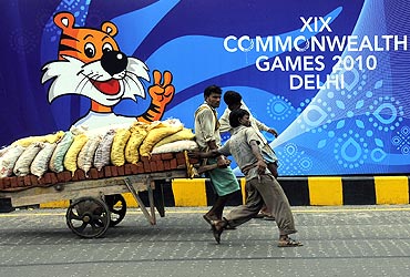 Labourers pull a hand cart loaded with bricks and sacks of sand in front of boards advertising the 2010 Commonwealth Games, over a flyover, in New Delhi