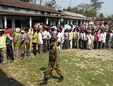 A policeman walks past people standing in a queue as they wait for their turn to cast their votes outside a polling station