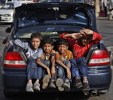 Boys sit in the trunk of a car while travelling on a street in Karachi