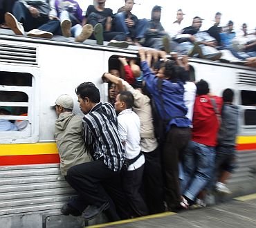 People hang onto an entrance of a commuter train which will transport them to Jakarta, in Depok, Indonesia's West Java province