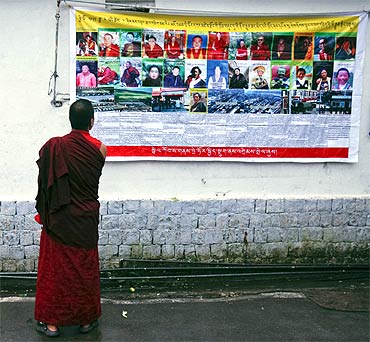 A Tibetan monk looks at a banner displaying pictures of what it said were Tibetan political prisoners in China, outside a monastery in Dharamsala