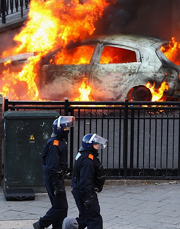 Police walk past a burning car during riots