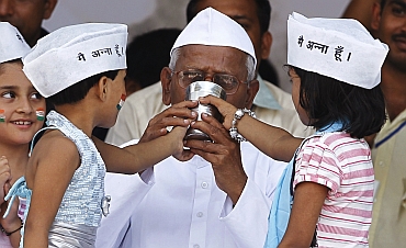 Simran (2nd L) and Ikra wearing traditional caps offer coconut water and honey to Hazare