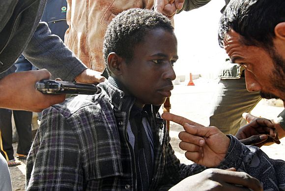 Rebels hold a young man at gunpoint, who they accuse of being a loyalist to Libyan leader Muammar Gaddafi, between the towns of Brega and Ras Lanuf, March 3, 2011