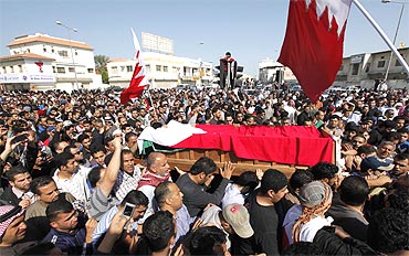 People carry the body of a protester killed during a protest on Monday, as they gather at a Shi'ite village cemetery in Sanabis