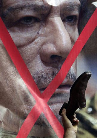 A Libyan protester uses a shoe to hit a crossed-out picture of Libyan leader Muammar Gaddafi