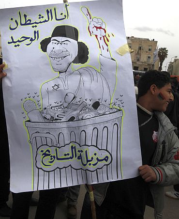 An anti-government protester holds a banner depicting Libyan leader Muammar Gaddafi in Benghazi city, Libya, on February 23. The characters read 'I am the only devil' (top) and 'the waste bin of history'