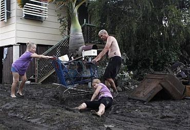 A girl falls in the mud as her sister and father remove damaged belongings from their home affected by floodwater in Bundaberg, Queensland