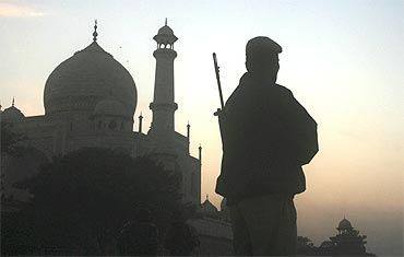 A police personnel stands guard behind the Taj Mahal during sunset in Agra