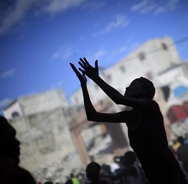A woman raises her arms for products as people loot a destroyed shop in Port-au-Prince