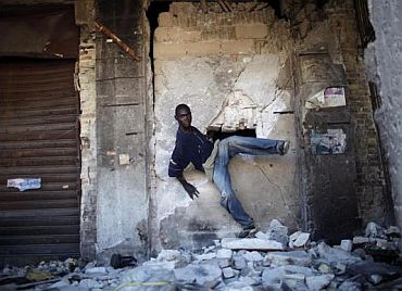 A looter leaves a damaged building through a hole in a wall in downtown Port-au-Prince