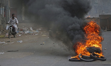 A man rides a motorcycle through the smoke of tyres burnt by angry protesters against target killing in Karachi
