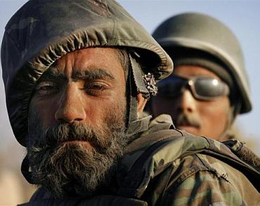 A dust-covered Afghan National Army soldier with a flower tucked behind his ear rides on the back of a vehicle during a patrol near Panjwaii town
