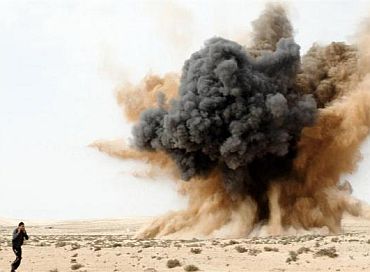 A rebel holds his ears as a bomb launched by a Libyan air force jet loyal to Libya's leader Muammar Gaddafi explodes in the desert near Brega