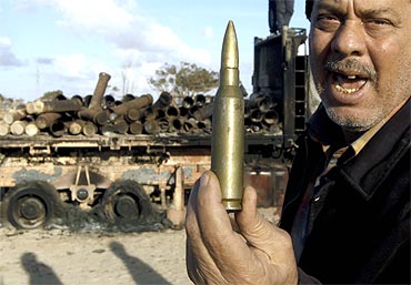A man holds up a round of ammunition at the road between Benghazi and Ajdabiyah