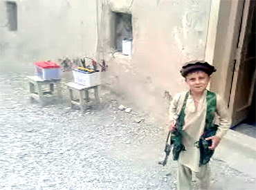 A child smiles while carrying a weapon in an undisclosed location in Pakistan's northwest region