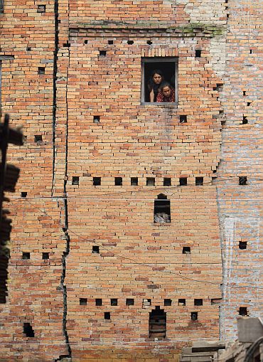 Women look out from the window of a quake-damaged house at Bhaktapur in Nepal