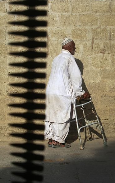 A man uses a walking frame as he walks through the street during a firefight between police and gang members in Karachi