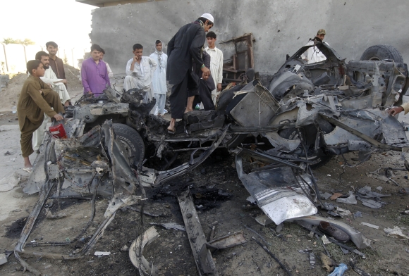 Afghan men stand around the wreckage of a car used by a suicide attacker in Jalalabad province