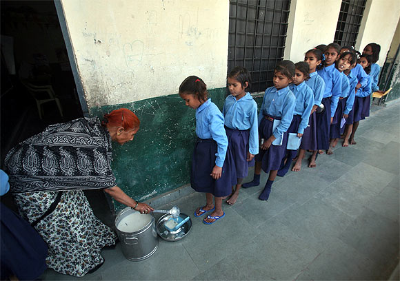 Children stand in line to collect their free mid-day meals in school