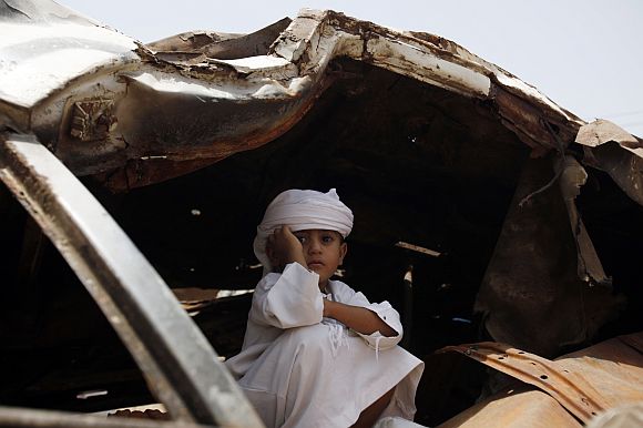 A boy takes shelter from the sun in the wreckage of a car destroyed during recent violence as he attends a rally to demand the ouster of Yemen's President Ali Abdullah Saleh in the southern city of Taiz
