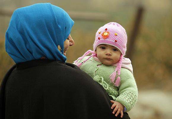 A woman walks while carrying her eight-month-old baby girl on a cold morning in Srinagar