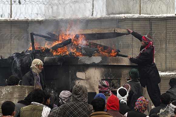 Afghan men stand near pieces of wood and tyres which they set on fire during a protest outside the U.S. military base in Bagram, north of Kabul February 21. More than 2,000 Afghans protested outside the main US military base in Afghanistan on Tuesday over a report that foreign troops had improperly disposed of copies of the Quran and other religious items, Afghan officials said.