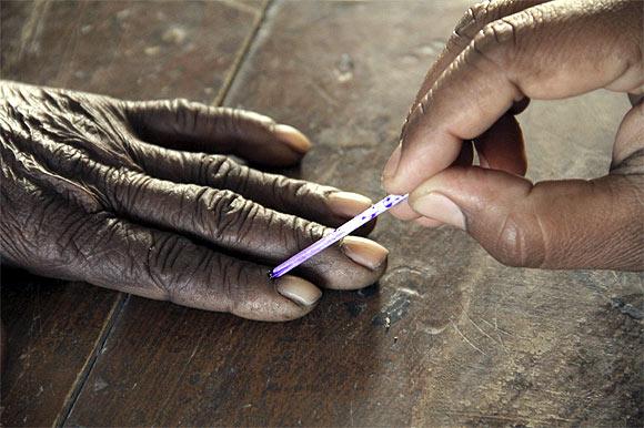 A voting official marks the finger of a voter inside a polling booth in UP