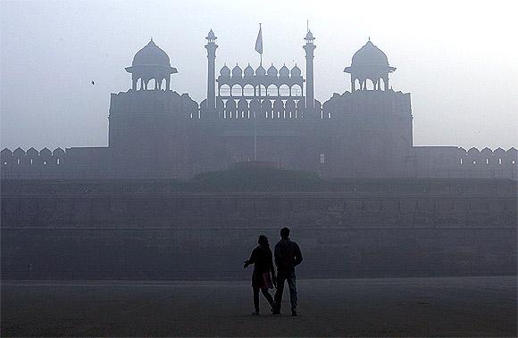 A couple walks in front of the historic Red Fort amid dense fog on a cold winter morning in the old quarters of Delhi