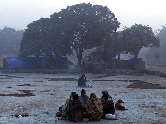 Men sit around a fire to warm themselves in a dried pool amid dense fog on a cold winter morning in the old quarters of Delhi