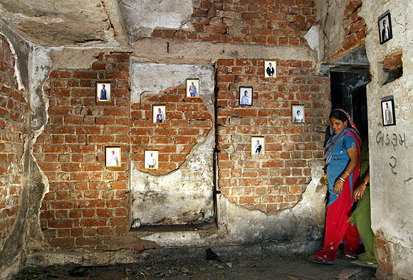 A survivor stands next to pictures of her family members inside her house that was burnt and damaged during the Gujarat riots in 2002